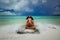 Beautiful little pirate girl making funny angry face, sitting on the tropical beach against tranquil ocean and dark dramatic sky