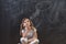 Beautiful little school girl sitting pensive in front of a blackboard in classroom at school