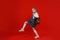 a beautiful little schoolgirl in a denim dress with a backpack on her shoulders walks on a red isolated background.