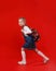 a beautiful little schoolgirl in a denim dress with a backpack on her shoulders walks on a red isolated background.