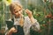 A beautiful little teenage girl with a tablet in her hands examines a sample of a plant through a magnifying glass