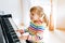 Beautiful little toddler girl playing piano in living room. Cute preschool child having fun with learning to play music