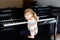 Beautiful little toddler girl playing piano in living room. Cute preschool child having fun with learning to play music