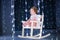 Beautiful little toddler girl in a white rocking chair in a dark room with Christmas lights