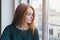 Beautiful lonely sad thoughtful pensive young girl sitting next to the window at home