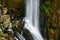 Beautiful long exposure photo of a waterfall rushing down a cliff and bursting onto a steep rocky mountainside