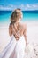 Beautiful long hair bride in long white dress standing on the beach with white bouquet loking to the sea