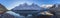 Beautiful long panorama of high rocky mountains with mighty glaciers and snowy peaks against the blue sky and clouds