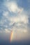 Beautiful long rainbow arc through fluffy white clouds and into