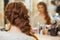 Beautiful, with long, red-haired hairy girl, hairdresser weaves a French braid, in a beauty salon.