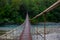 Beautiful, long suspension bridge over a mountain river, going into a dense forest