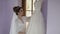 Beautiful and lovely bride in night gown stands near wedding dress. Wedding morning. Pretty and well-groomed woman. Slow motion
