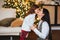 Beautiful loving mom gently kissing little daughter against festively decorated xmas tree at home