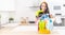 Beautiful maid standing in the kitchen, with a bucket full of colorful cleaning stuff in front of her, wearing rubber gloves