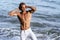 Beautiful man with naked muscular torso at white sand beach.