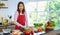 Beautiful mature adult Asian female housewife in apron standing in kitchen with various kinds and colorful vegetables and fruit