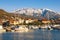 Beautiful Mediterranean landscape on sunny winter day. Fishing boats in harbor at foot of snowy mountains. Montenegro, Tivat