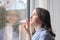 Beautiful melancholic teenager girl in light blue shawl  looking outside through raindrops on wet window