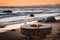 The beautiful metal round a fireplace stands on the sandy coast with a tidal wave at sunset, stones, sand, waves, the