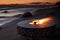 The beautiful metal round a fireplace stands on the sandy coast with a tidal wave at sunset, stones, sand, waves, the