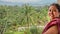 Beautiful mexican woman who is on a balcony with palm trees and mountains in the background