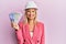 Beautiful middle age blonde woman wearing architect hardhat holding indian rupee looking positive and happy standing and smiling