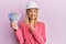 Beautiful middle age blonde woman wearing architect hardhat holding indian rupee smiling happy pointing with hand and finger