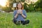 Beautiful middle-aged woman sitting on grass in garden, relaxing at sunset