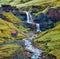 Beautiful midnight sun view of nameless waterfall on Rauda river. Vivid green hills on the southern coast of Iceland at June.