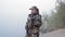 Beautiful military woman in army camouflage drinks hot tea holding a metal mug on the background of the river in the fog