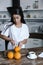 Beautiful mixed race girl in white robe preparing orange juice in morning and cutting oranges