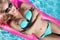 Beautiful model model with long blonde wet hairs, sunglasses and bikini swims in the pool on a pink mattress ,