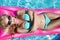 Beautiful model model with long blonde wet hairs, sunglasses and bikini swims in the pool on a pink mattress ,