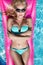 Beautiful model model with long blonde wet hairs, sunglasses and bikini swims in the pool on a pink mattress ,