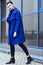 Beautiful model with perfect make up and hair scrapped back into a bun walking in trendy blue coat