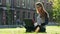 Beautiful and modern female student or freelancer working on a laptop, redhead woman sitting in a park on green lawn in