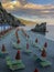 Beautiful Monterosso al Mare, Italy beach at sunset. Orange and green beach chairs, umbrellas across sunset sky, rocks, and mounta