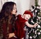Beautiful mother with luxurious dark hair posing with her cute little girl beside Christmas tree