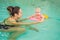 Beautiful mother teaching cute baby girl how to swim in a swimming pool. Child having fun in water with mom