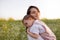 Beautiful motherhood, young pretty mother with closed eyes embraces a daughter, toddler, baby, on hands, on field, nature