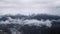 Beautiful mountain landscape with snowy peaks and low clouds. Cloudy low sky overhanging snowy peaks of wooded mountains