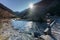 Beautiful mountain stream and peak landscape with the sun shining and a wooden bridge with a hiking trail sign in the foreground