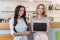 Beautiful multiethnic waitresses with blank board looking at camera while standing at cafe