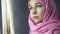 Beautiful muslim arabian woman in pink hijab looking out the window