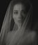 Beautiful mysterious woman face in darkness covered white veil on dramatic shadow black background. Closeup emotion studio