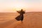 Beautiful mysterious woman in traditional arabic black long dress stands in the desert on sunset