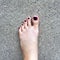 Beautiful Nail, Close Up Woman`s Bare Feet and Red Nail Polish on Cement Floor Background