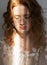 Beautiful natural redhead girl bride, with nude makeup, wearing a white dress, poses in the shadow, illuminated by a narrow beam
