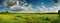 Beautiful natural scenic panorama green field of cut grass into and blue sky with clouds on horizon.