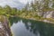 Beautiful nature landscape view of rain drops on pond surface. Rocky coast and tall pine trees on pale sky background.